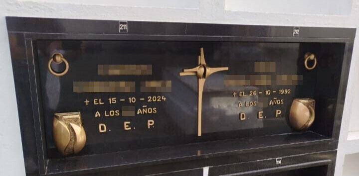 Lápida doble de granito negro con inscripción, floreros y cruz en bronce