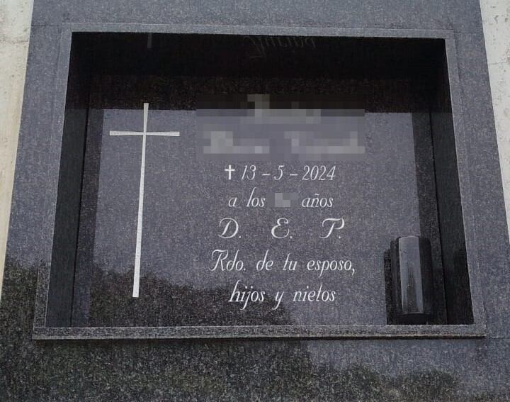 Lápida en granito negro con inscripción y cruz grabada pintada en blanco y búcaro